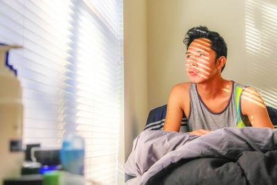 Man looking away on bed in sunny day