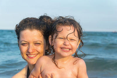 Portrait of smiling mother and daughter against sea