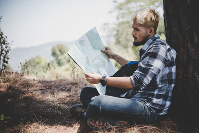 Side view of young man reading map while sitting on field