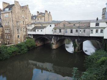 Arch bridge over river by buildings against sky