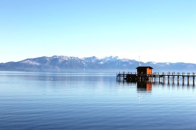 Pier and stilt house at lake by mountains against clear blue sky