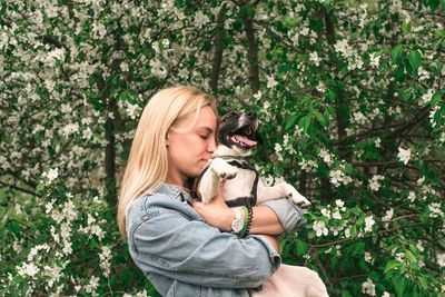 Woman carrying dog while standing against trees in park