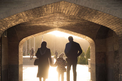 Rear view of people walking through tunnel in city