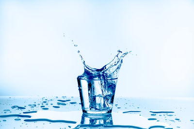 Close-up of water splashing on glass against white background