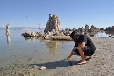 Woman standing on rock at beach against clear sky