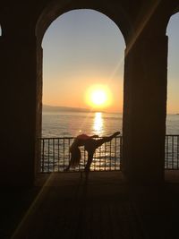 Silhouette person by sea against sky during sunset