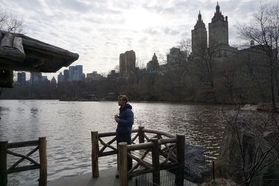 Man standing on pier by lake against skyscraper in city