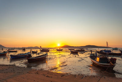 Boats moored in water at sunset