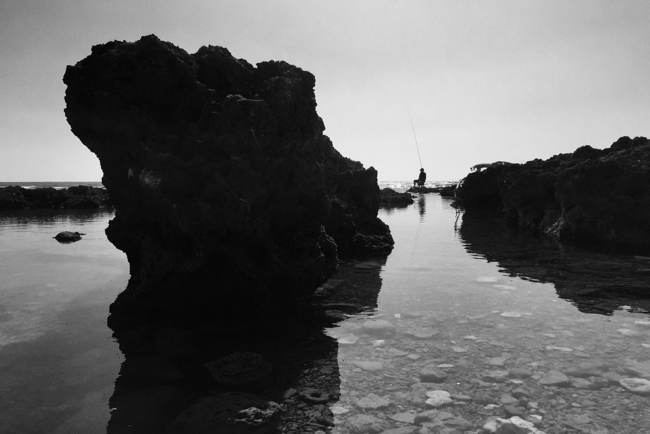 water, sea, clear sky, reflection, tranquility, rock - object, sky, tranquil scene, built structure, nature, the way forward, scenics, beauty in nature, rock formation, copy space, outdoors, architecture, day, waterfront, rock