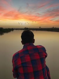 Rear view of man by lake against dramatic sky