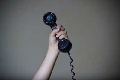 Cropped hand of woman holding telephone against wall