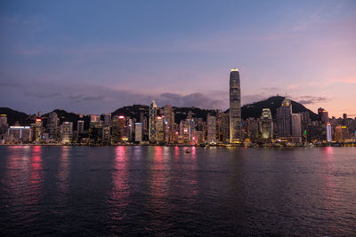 Illuminated buildings by sea against sky at night