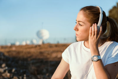 Young woman wearing headphones against sky