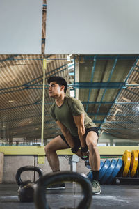 Asian man training shoulders and arms with heavy kettlebells in gym during functional workout and looking away