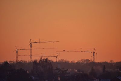 Silhouette of cranes against sky during sunset