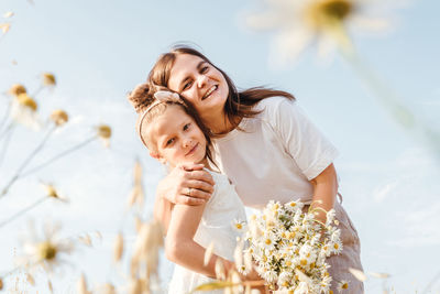 Portrait of mother and daughter by plants against sky