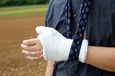 Midsection of man wearing bandage on injured hand while standing on land