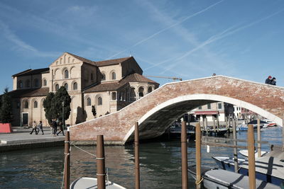 Bridge over canal by buildings against sky