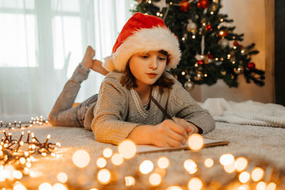 New year's and christmas. a teenage girl in a santa claus hat writes a letter to santa claus 