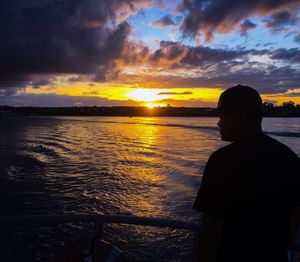 Silhouette man standing by sea against sky during sunset