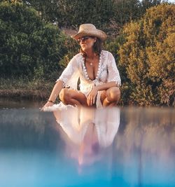 Woman sitting by lake against trees