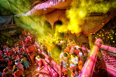 A hindu priest throws colourful powders over devotees inside radhaballav temple of vrindavan .