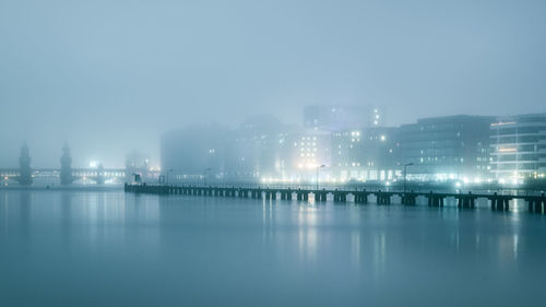 Illuminated city by sea against sky at night