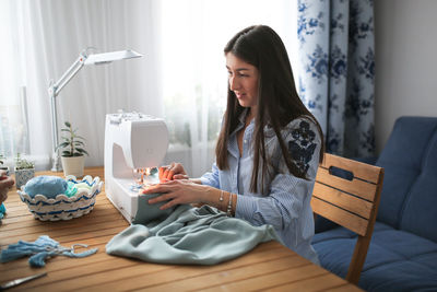 Beautiful woman with long dark hair sews a blue cloth on a sewing machine. 