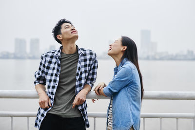 Smiling couple standing by railing against sky