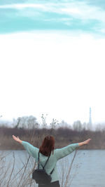 Rear view of woman with arms raised against sky