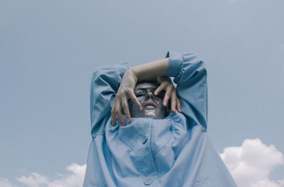 Low angle view of woman holding blue umbrella against sky