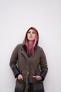 Young woman in pink hair standing against wall
