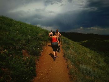 Rear view of friends walking on mountain trail against cloudy sky