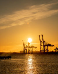 Silhouette cranes at pier against sky during sunset