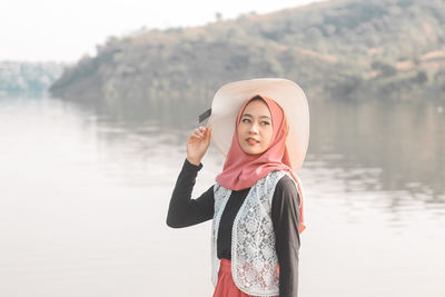 Portrait of young woman standing against lake