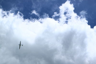 Low angle view of glider flying in cloudy sky