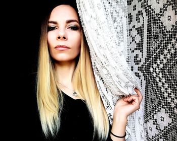 Portrait of beautiful young woman standing by curtain