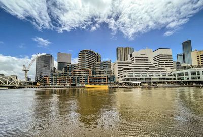 City buildings by river against sky and clouds.