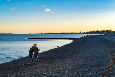 Rear view of friends walking at beach during sunset