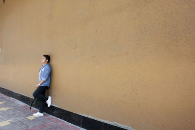 Young man leaning on orange wall