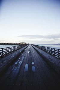 Surface level of wooden walkway against clear sky