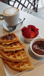 Brunch with delicious cappuccino and waffles accompanied by strawberry and hazelnut cream.