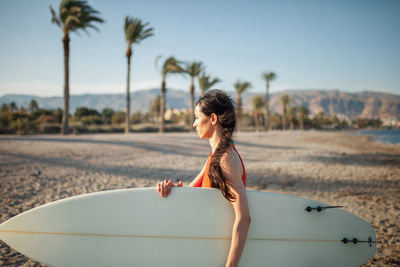 Side view of woman carrying surfboard while walking at beach