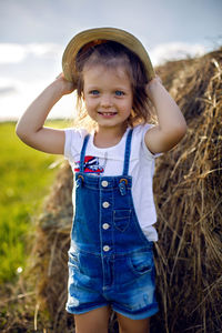 Little girl in the haystack in a hat and denim overalls