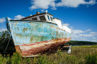 Abandoned boat on grass against sky