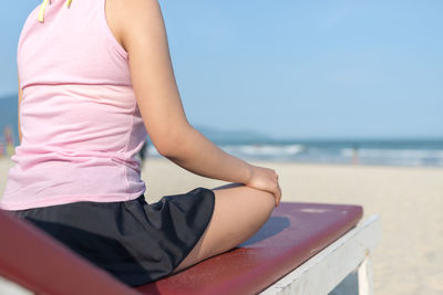 Midsection of woman sitting on beach against sky