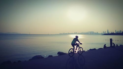 Person cycling by sea during sunset