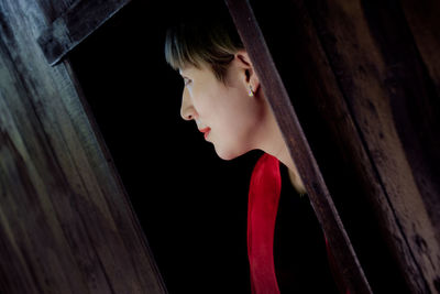 Close-up of woman looking away while standing by wooden wall