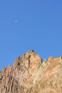 Low angle view of rocky mountains against clear blue sky