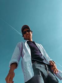 Low angle view of young man wearing sunglasses standing against blue sky